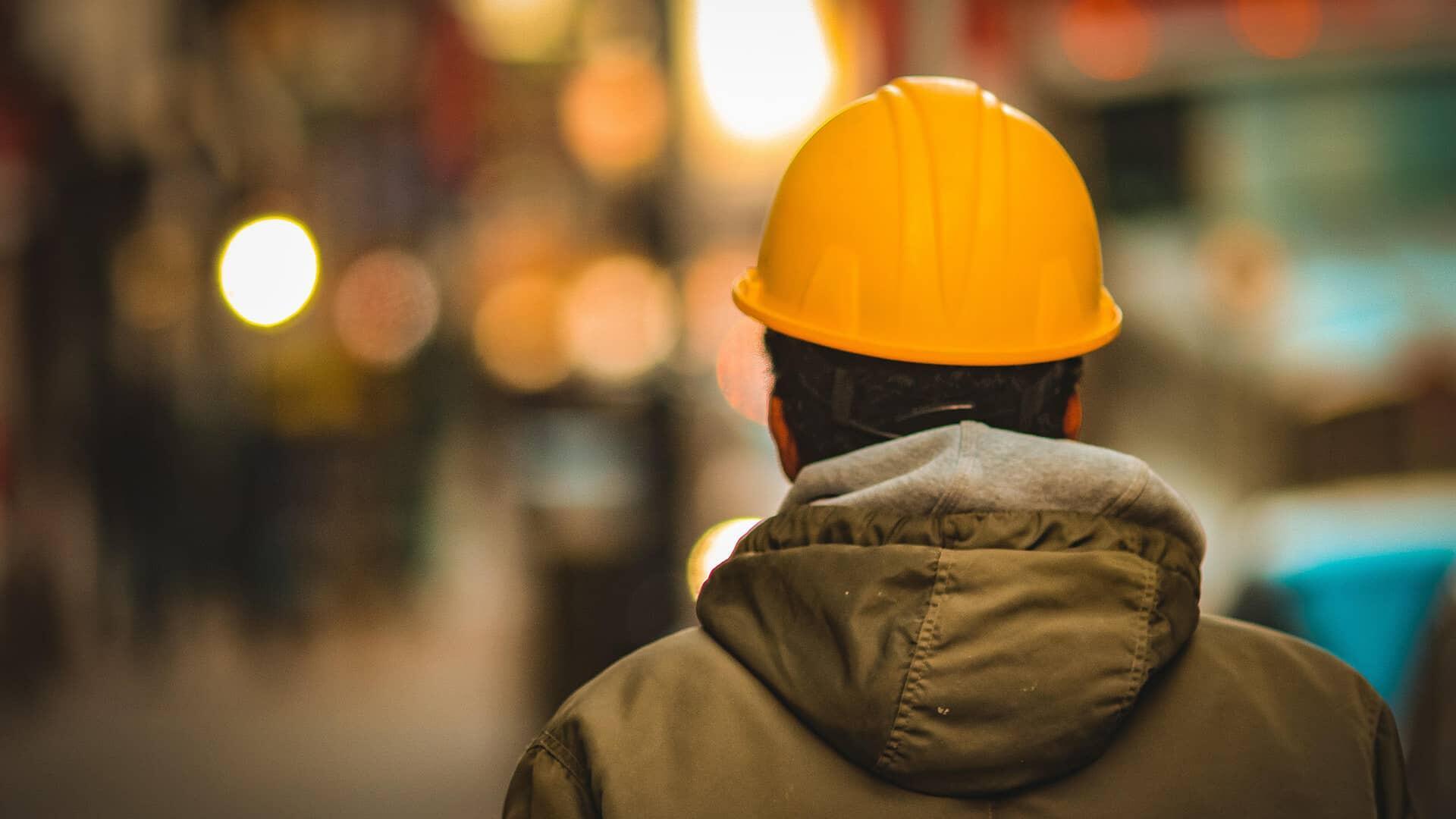 Un homme de dos avec un casque de chantier sur un fond flouté