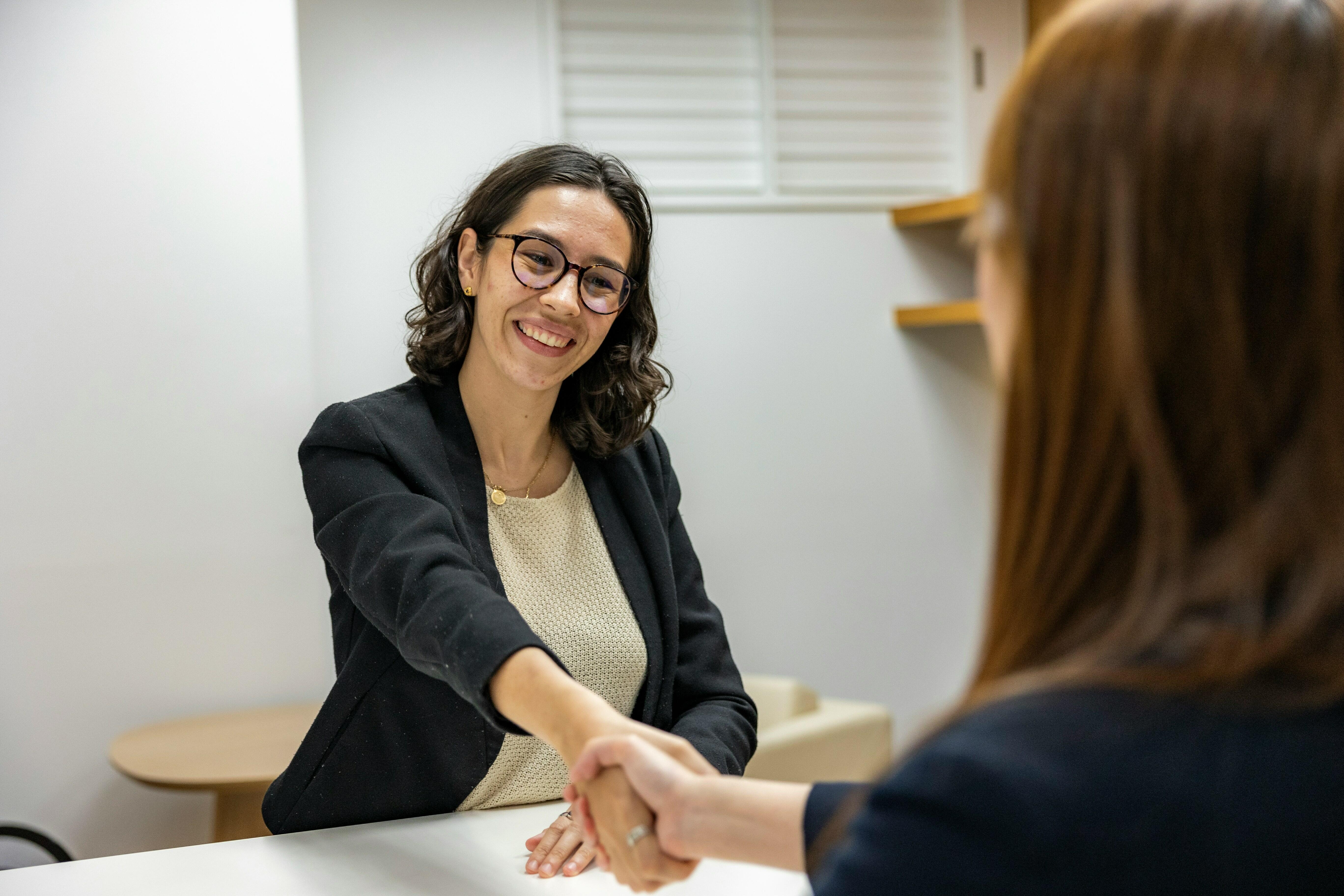 une femme serrant la main dune autre femme assise a une table